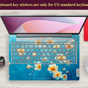 May include: A laptop computer with a blue and white floral keyboard sticker. The sticker features a design of white flowers with yellow centers on a blue background. The text "Keyboard key stickers are only for US standard keyboards" is displayed at the top of the image.