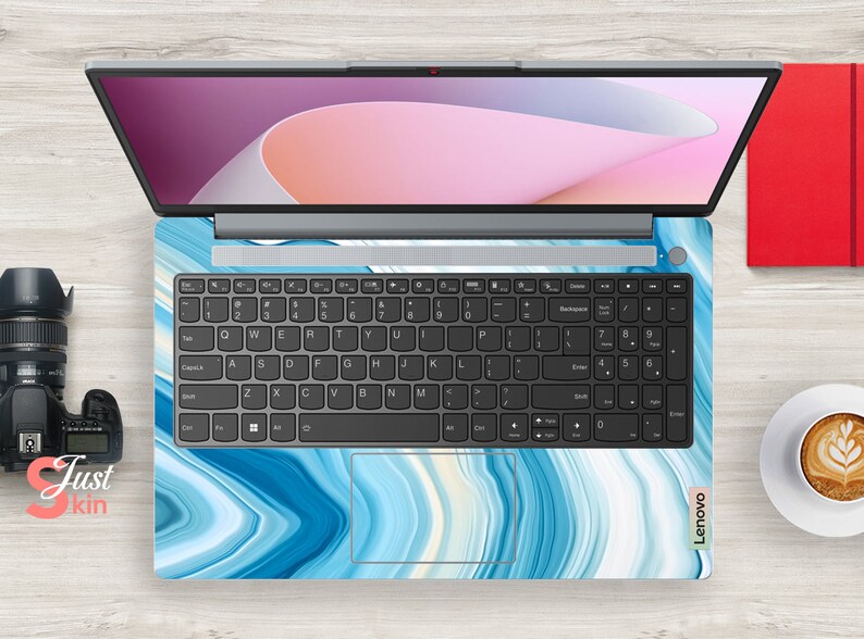 Op de afbeelding: Een laptop met een blauwe en witte marmer-design skin. De laptop heeft een zwart toetsenbord en een zilveren frame. Het scherm toont een roze en wit abstract ontwerp.