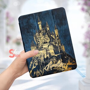 Puede incluir: Una funda para tablet azul y dorada con una ilustración de un castillo y el nombre "Amelia" escrito en letras doradas.