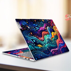 Puede incluir: Un port&aacute;til Lenovo con una llamativa funda abstracta con patrones ondulados en tonos azules, morados, naranjas y amarillos. La funda cubre la tapa y el &aacute;rea del teclado, creando un dise&ntilde;o cohesivo. El texto "Just Skin" es visible.