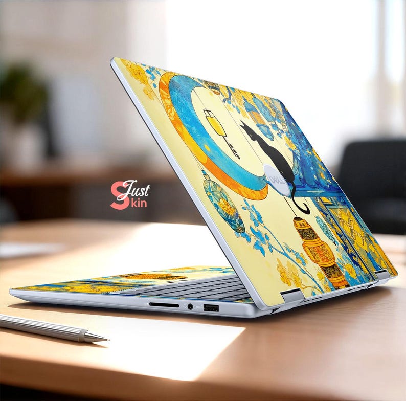 May include: A laptop with a decorative skin featuring a black cat, lanterns, and floral elements in yellow and blue. The laptop is open on a wooden surface, with the text "Just kin" visible.