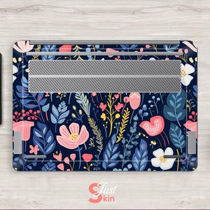Op de afbeelding: Een laptop skin met een bloemenpatroon van roze, witte en gele bloemen en blauwe bladeren op een marineblauwe achtergrond. Het heeft een zilverkleurig ventilatiegedeelte. Een tablet met een bijpassend ontwerp is ook zichtbaar.