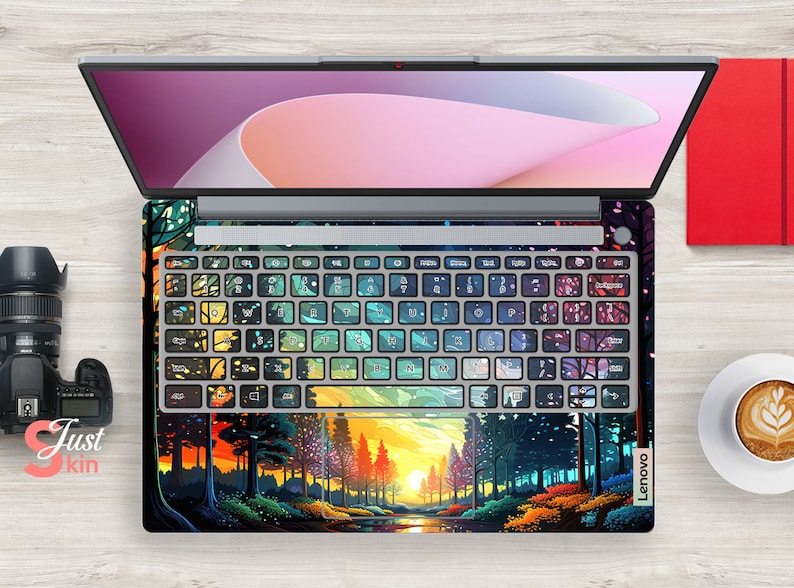 K&ouml;nnte beinhalten: Ein Laptop mit einem farbenfrohen Waldmotiv und Sonnenuntergang auf der Tastatur und dem Trackpad. Das Design zeigt eine Vielzahl von Farben, darunter Gr&uuml;n, Blau, Lila und Gelb. Der Laptop ist ge&ouml;ffnet und der Bildschirm ist ausgeschaltet. Der Laptop steht auf einer Holzoberfl&auml;che.