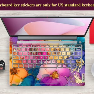 May include: Laptop with a colorful floral design keyboard skin and key stickers. The keyboard skin features a vibrant mix of orange, purple, and blue hues with gold accents. The text on the image says "Keyboard key stickers are only for US standard keyboards."