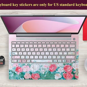 Peut inclure: Un ordinateur portable avec un autocollant de clavier floral. L'autocollant pr&eacute;sente des fleurs roses, blanches et vertes sur un fond rose clair. L'ordinateur portable est ferm&eacute; et l'&eacute;cran affiche un fond rose et blanc.