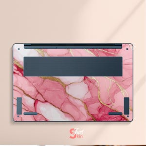 Op de afbeelding: Laptop skin met een roze marmerontwerp en gouden aders. De skin heeft een donkerblauwe ventilatiezone en hoekaccenten. De tekst "Just kin" is rechtsonder zichtbaar.