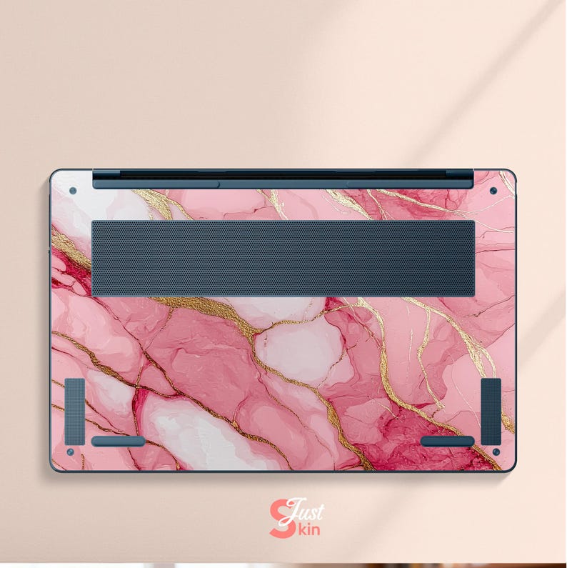 Op de afbeelding: Laptop skin met een roze marmerontwerp en gouden aders. De skin heeft een donkerblauwe ventilatiezone en hoekaccenten. De tekst "Just kin" is rechtsonder zichtbaar.