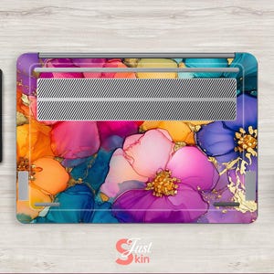May include: A laptop skin featuring a vibrant floral design in shades of purple, pink, orange, and blue with gold accents. The design is abstract and artistic, with a watercolor effect. The laptop skin is on a wooden surface.