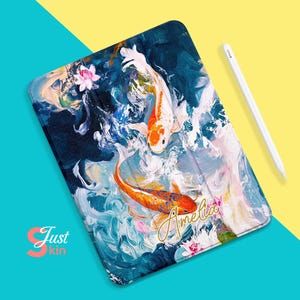 Puede incluir: Una funda para iPad azul y blanca con un diseño de acuarela de dos peces koi y flores rosas. El nombre "Amelia" está escrito en letras doradas en la funda.