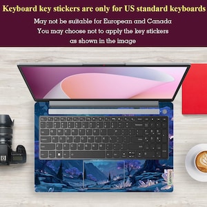 K&ouml;nnte beinhalten: Ge&ouml;ffnetes Laptop mit einer Tastaturfolie mit einem blauen und violetten Landschaftsdesign. Die Tastatur hat schwarze Tasten. Das Bild enth&auml;lt eine Kamera, ein rotes Notizbuch und eine Tasse Kaffee. Der Text besagt, dass die Tastaturaufkleber nur f&uuml;r US-Tastaturen geeignet sind.