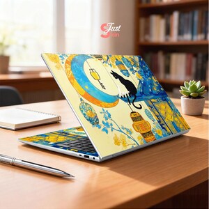 May include: Laptop with a decorative skin featuring a black cat perched on a crescent moon. The design includes yellow lanterns, blue floral accents, and a yellow background. The laptop is open on a wooden desk.