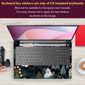 May include: Laptop with a decorative keyboard skin featuring a dark floral design with gold and white accents. The laptop is open, displaying the keyboard and screen. Text on the image states that the keyboard key stickers are only for US standard keyboards.