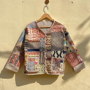 Puede incluir: Una chaqueta acolchada de patchwork con cierre de botones y mangas largas. La chaqueta está hecha de una variedad de telas en diferentes colores y patrones, incluyendo azul, rojo, marrón y blanco.