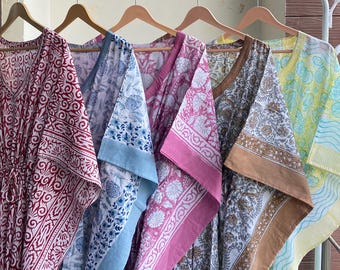 May include: A row of five colorful, patterned kaftans hanging on a white rack. The kaftans feature various designs in shades of red, blue, pink, brown, and yellow. Each kaftan has a V-neck and short sleeves, perfect for warm weather.