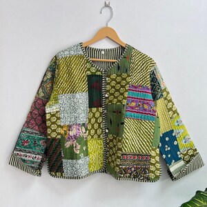 Könnte beinhalten: Eine grüne Patchwork-Steppjacke mit V-Ausschnitt und langen Ärmeln. Die Jacke besteht aus verschiedenen Stoffen mit floralen und geometrischen Mustern.