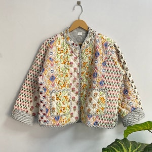 May include: A white quilted jacket with a floral print. The jacket has a stand-up collar, long sleeves, and a zip closure. The fabric is a patchwork of different floral patterns in shades of pink, blue, yellow, and green.