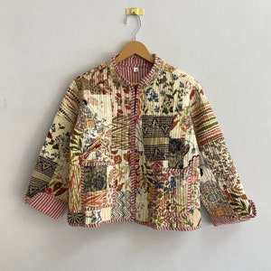 May include: A cream-colored quilted jacket with a floral patchwork design. The jacket has a mandarin collar, long sleeves, and a front zipper closure. The fabric is a mix of different floral prints in shades of red, blue, green, and brown.