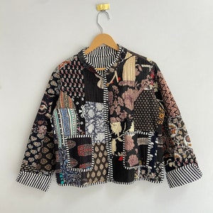 Może przedstawiać: Czarna pikowana kurtka z patchworkowym wzorem, który zawiera różne wzory kwiatowe i geometryczne w odcieniach brązu, niebieskiego, czerwonego i białego.