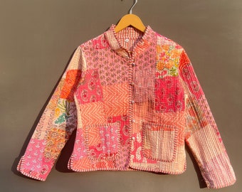 Può includere: Una giacca trapuntata rosa con un design a patchwork. La giacca ha un colletto alla coreana, maniche lunghe e una chiusura con bottoni. Il tessuto è un mix di motivi floreali e geometrici.