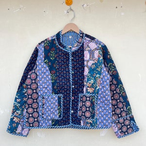 Puede incluir: Una chaqueta acolchada azul y verde con estampado floral. La chaqueta tiene un cuello mandarín, cierre de botón y dos bolsillos de parche.