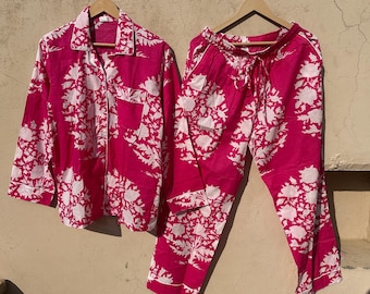Op de afbeelding: Een roze en witte pyjamaset met een bloemenprint, bestaande uit een shirt met lange mouwen en een broek.