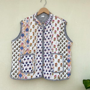 Puede incluir: Un chaleco acolchado sin mangas blanco con estampado floral y ribete negro. El chaleco tiene un cuello mandarín y cierre de botón.