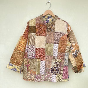 Puede incluir: Una chaqueta de patchwork marrón, beige y morado con cuello mandarín y cierre de botón.
