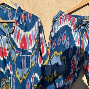 May include: A blue and white patterned pajama set with a long-sleeved shirt and pants. The pattern features abstract shapes in shades of blue, white, red, and yellow.