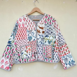Puede incluir: Una chaqueta de algodón blanca con un diseño de patchwork que presenta patrones florales y geométricos en tonos de rosa, azul, verde y naranja. La chaqueta tiene un cierre de botón y una textura acolchada.
