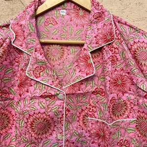 May include: Pink button-up shirt with a floral print and white trim. The shirt has a collar and a button closure. The size tag says "XXL".
