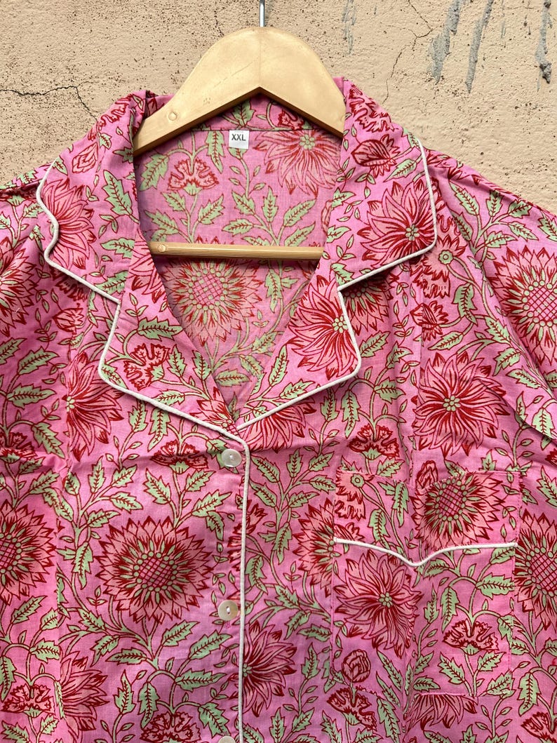 May include: Pink button-up shirt with a floral print and white trim. The shirt has a collar and a button closure. The size tag says "XXL".