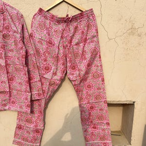 May include: Pink pajama pants with a floral print. The pants have a drawstring waistband and a white trim.