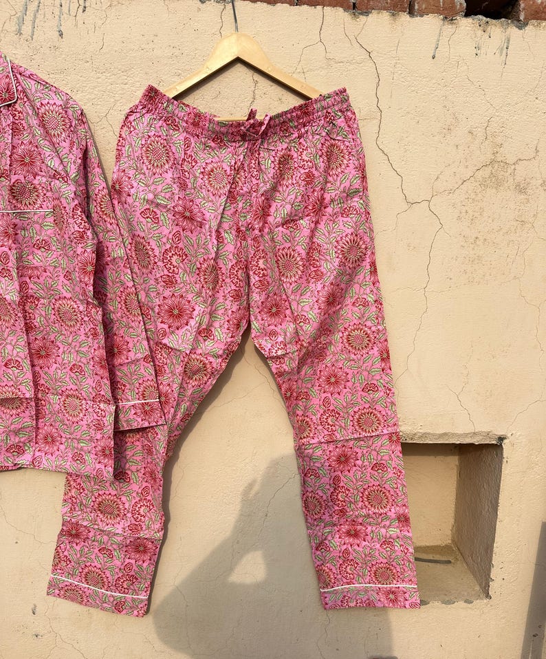 May include: Pink pajama pants with a floral print. The pants have a drawstring waistband and a white trim.