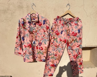 Può includere: Un pigiama rosa con stampa floreale. La parte superiore ha una chiusura con bottoni sul davanti e maniche lunghe. I pantaloni hanno una vita con coulisse e sono lunghi.