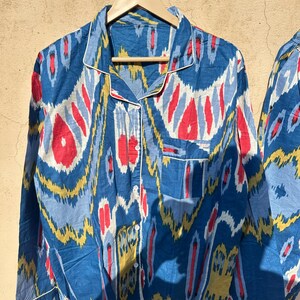May include: A blue and white patterned pajama top with red and yellow accents. The top has a button-up front and long sleeves.