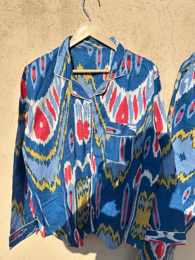 May include: A blue and white patterned pajama top with red and yellow accents. The top has a button-up front and long sleeves.