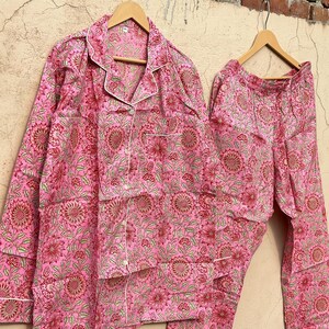 May include: Pink cotton pajama set with a floral print. The top has a button-up front and a collar. The pants have an elastic waistband.