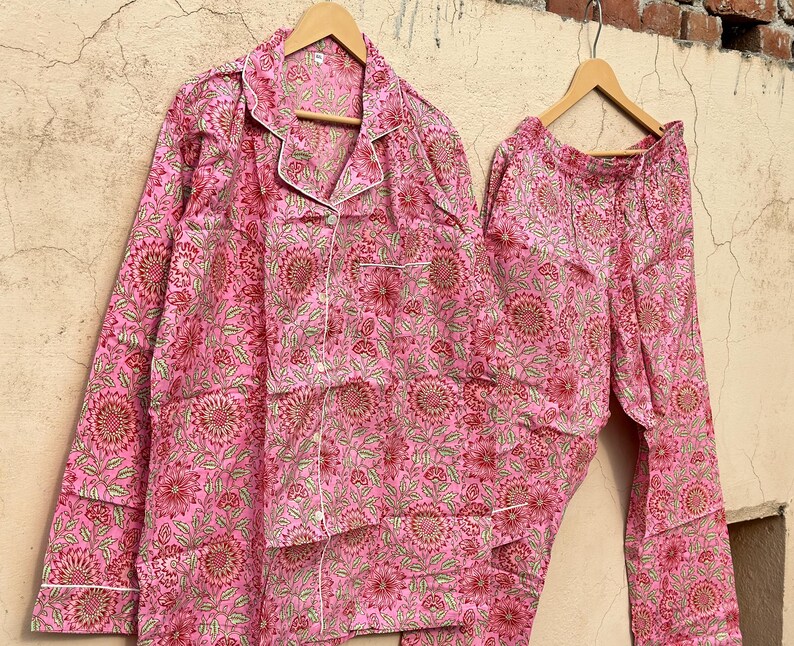 May include: Pink cotton pajama set with a floral print. The top has a button-up front and a collar. The pants have an elastic waistband.