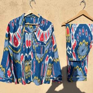 May include: A blue and white patterned pajama set with red and yellow accents. The top has a button-up front and long sleeves. The pants have a straight leg.