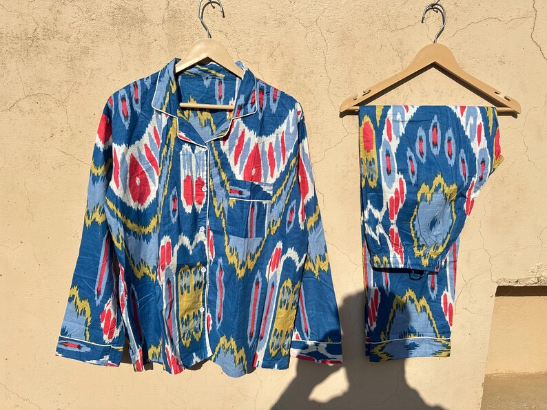 May include: A blue and white patterned pajama set with red and yellow accents. The top has a button-up front and long sleeves. The pants have a straight leg.