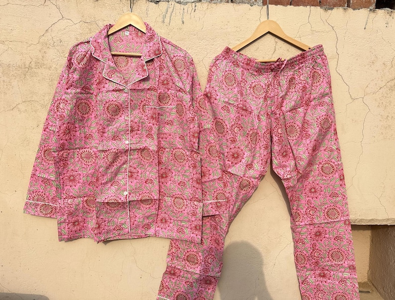 May include: Pink pajama set with a floral print. The top has a button-up front and the pants have an elastic waistband.