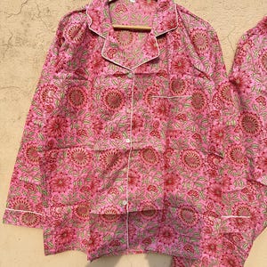 May include: Pink pajama set with a floral print. The top has a button-up front and long sleeves. The pants have an elastic waistband.