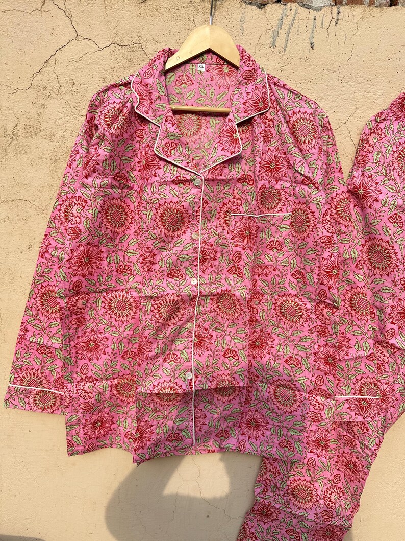 May include: Pink pajama set with a floral print. The top has a button-up front and long sleeves. The pants have an elastic waistband.