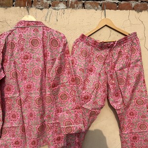 May include: Pink pajama set with a floral print. The top has long sleeves and a button-up front. The pants have a drawstring waist.