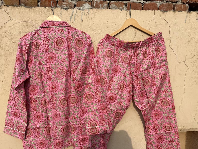May include: Pink pajama set with a floral print. The top has long sleeves and a button-up front. The pants have a drawstring waist.