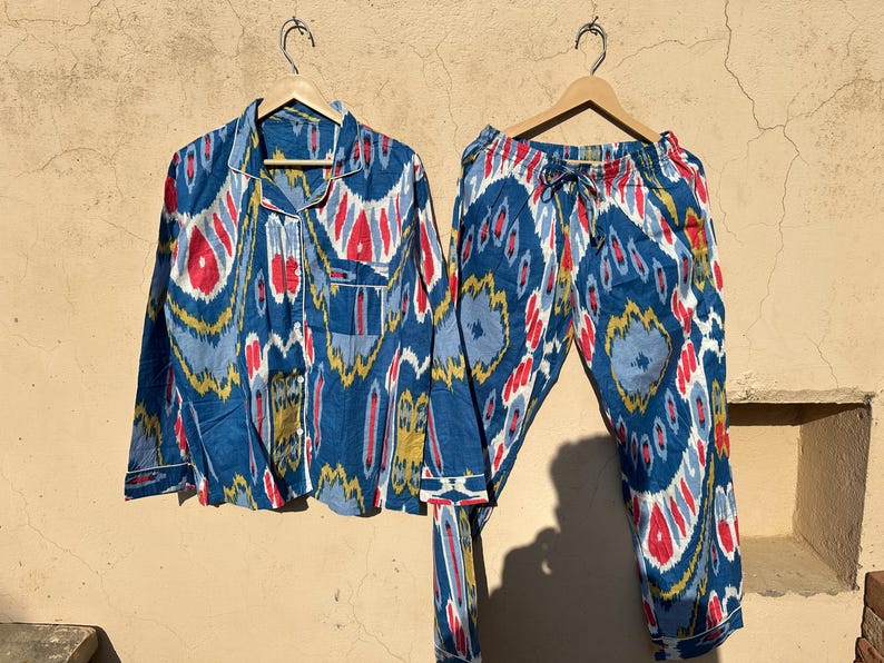 May include: A blue and white pajama set with a red, yellow, and blue ikat pattern. The set includes a long-sleeved shirt with a button-up front and matching pants with a drawstring waist.