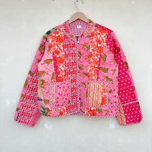 Peut inclure: Une veste matelassée rose avec un motif patchwork représentant des tigres, des fleurs et des motifs géométriques. La veste a un col mandarin, des manches longues et une fermeture boutonnée.