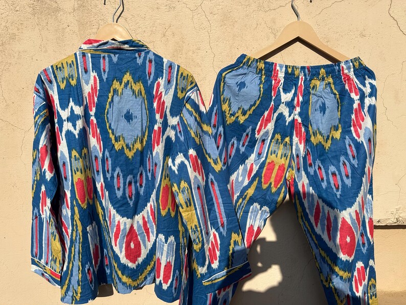 May include: A blue and white patterned pajama set with red and yellow accents. The top has a button-up closure and long sleeves. The pants have an elastic waistband.