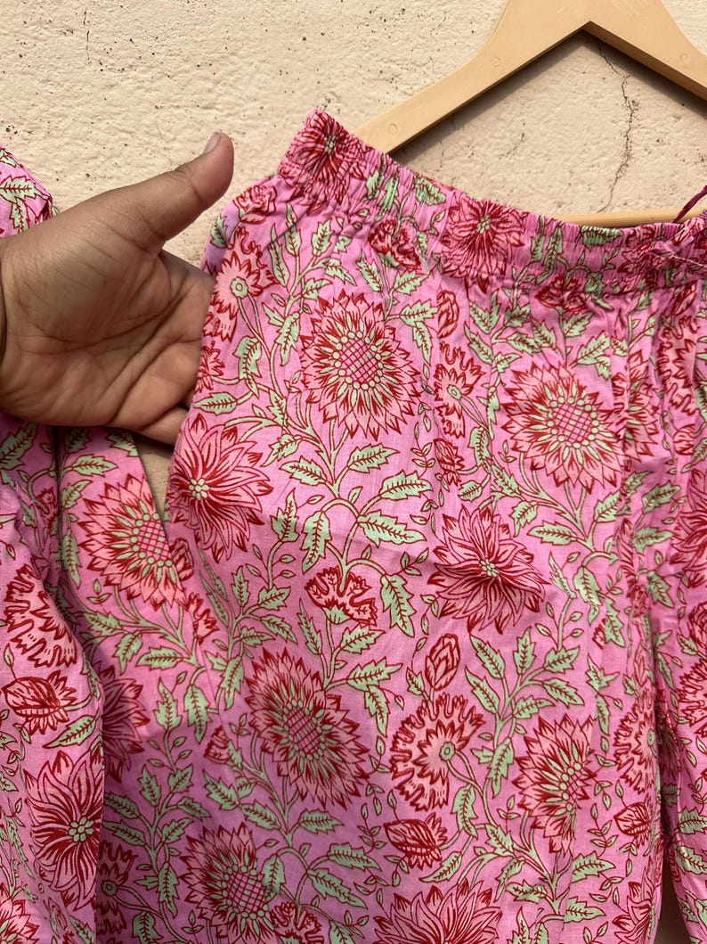 May include: Pink cotton pants with a floral print in shades of red and green. The pants have an elastic waistband.