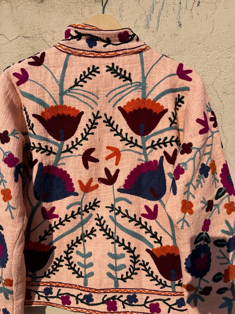 May include: A pink embroidered jacket with floral designs in shades of blue, red, orange, and green.